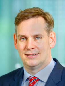 Kornelius Nielsch im Anzug vor türkisfarbenem Hintergrund.